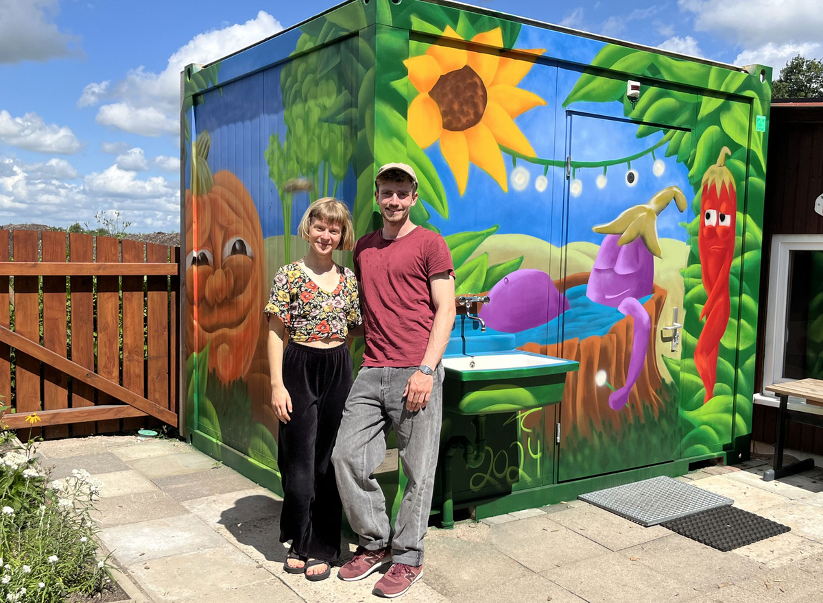 Die Künstler Kristina und Peter von againstgreywalls stehen vor dem farbenfroh fertig gestalteten Sanitär-Container